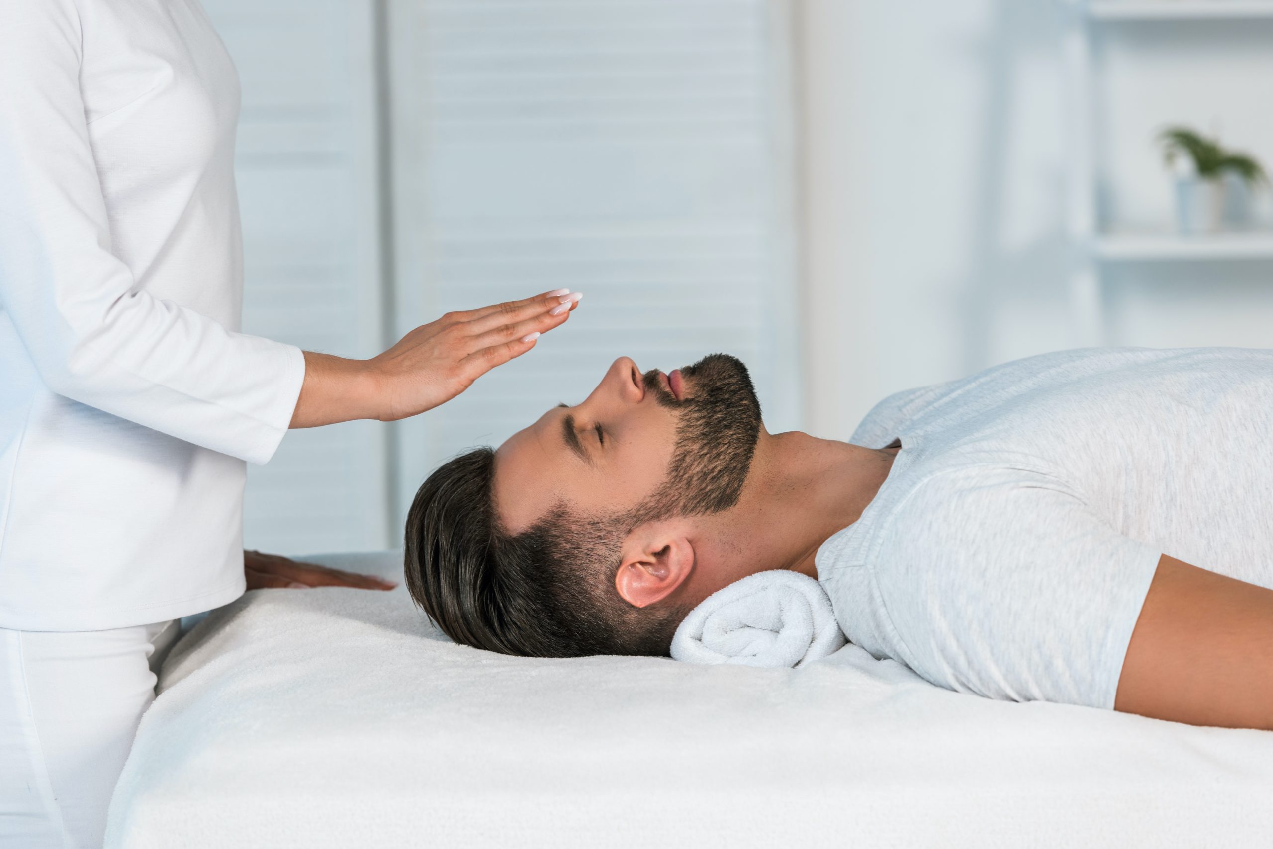 cropped view of healer putting hands above head of handsome man on massage table